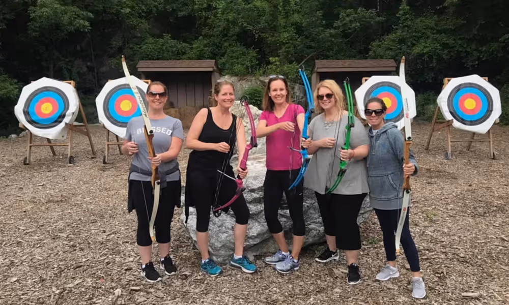 Five girlfriends holding bows at archery range. 