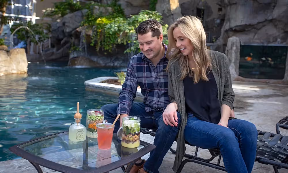 Woman and man sitting pool side in the Biosphere drinking cocktails and eating salads.