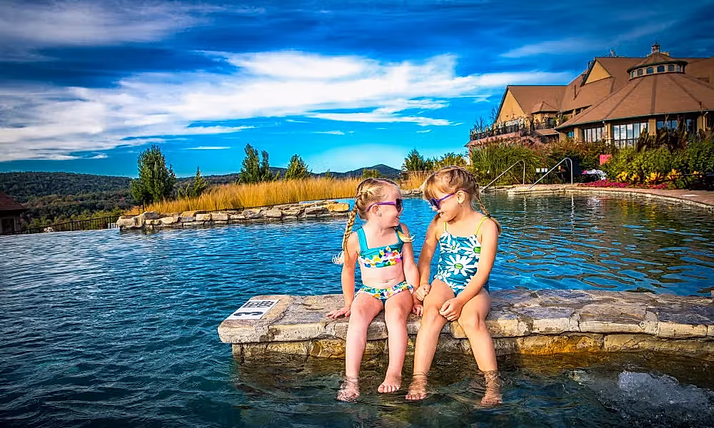 Two young girls wearing sunglasses and sitting at the Vista 180 pool.