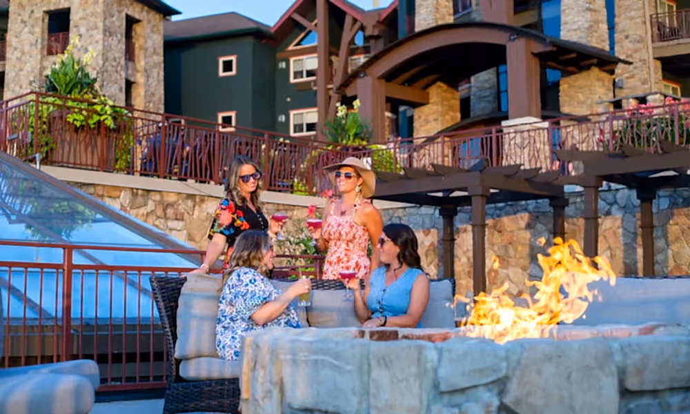 Group of four girlfriends sitting around firepit on Fire &amp; Water terrace.