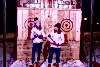 Two girls wearing white winter jackets and holding axes in their hands to throw.