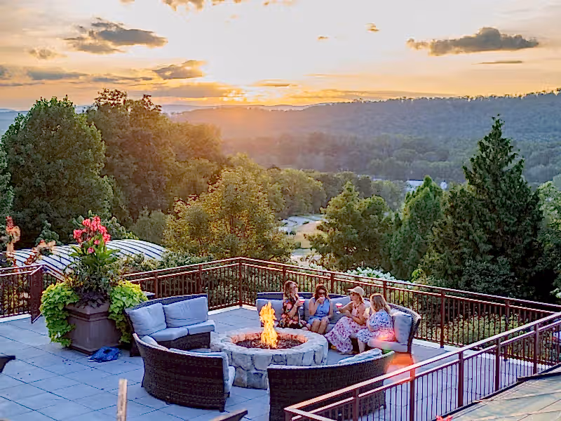 Group of four girlfriends sitting around firepit on Fire &amp; Water terrace overlooking sunset mountain views.